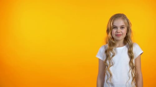 Glückliches entzückendes Mädchen, das lacht, auf orangefarbenem Hintergrund steht, Humor und W