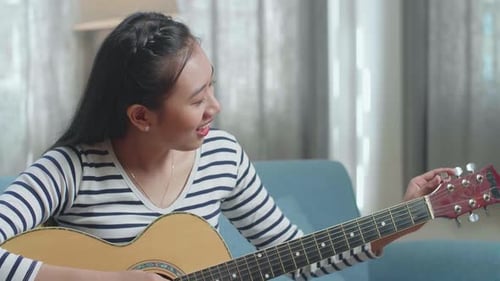 Gros plan d'une femme asiatique apprenant à tirer des cordes de guitare par un ordinateur portable à la maison
