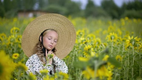 Beautiful Teen Girl in Straw Hat and Dress Posing on Sunflower Field at Summertime