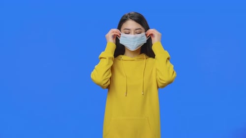 Woman puts on face mask in front of blue screen