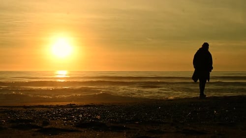 Frau geht allein am Strand entlang während des malerischen Sonnenuntergangs