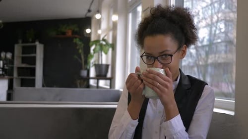 Portrait of Merry Dark Skinned Adolescent Into Spectacles Drinking Tea From Cup Close-up at Cafe Bar