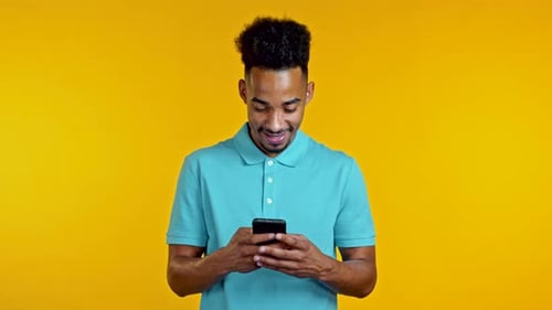 Handsome African Man Using Smartphone on Yellow Studio Wall. Using Modern Technology - Apps, Social