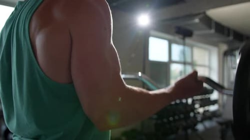A young man in the gym does a biceps exercise while lifting a barbell in front of him