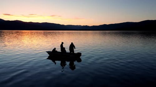 People Fishing in Boat on Lake at Sunset