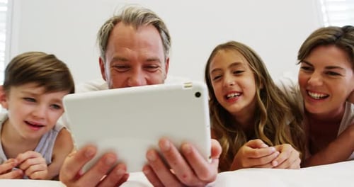 Happy Family Using Tablet Lying on Bed Together