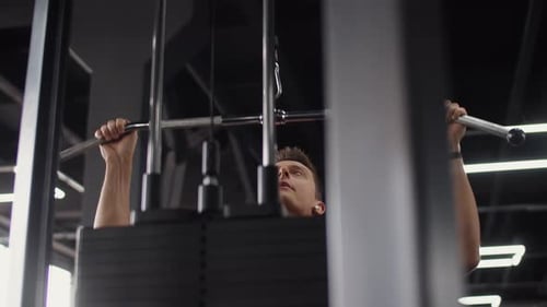 Man Bodybuilder with Headphones Training in Gym Lifting Heavy Weight on Exercise Machine Side View