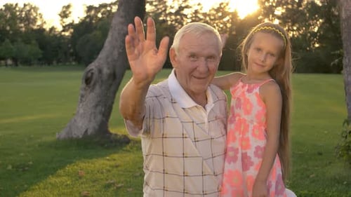 Grandfather and Granddaughter Waving in the Park at Sunrise