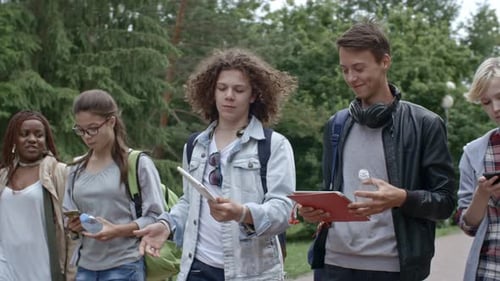 Teen Students Walking Through Park with Books and Tablets