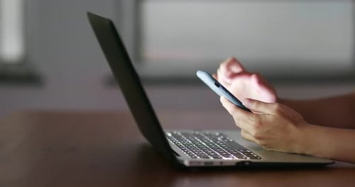 Hands Using Smartphone Next to Laptop