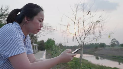 Asian woman chatting in smartphone to friend at outdoor landscape river