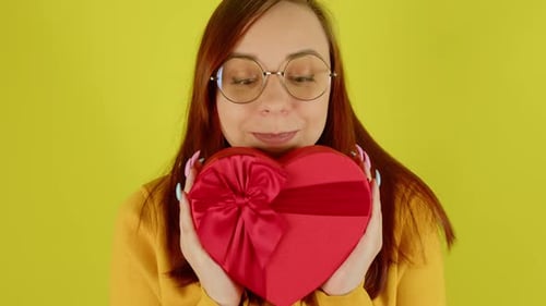 Young Woman Holding Heart Shaped Present on Yellow