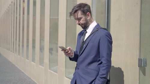 Elegant Young Businessman Using Phone to Text or Check Email in a Urban Office District