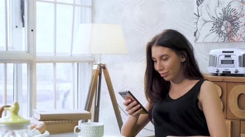Close Up View From The Side A Young Woman Is Sitting On A Chair In A Bright Kitchen Watching