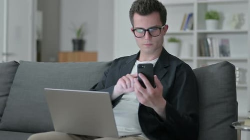 Young Male Designer Using Smartphone and Laptop at Home
