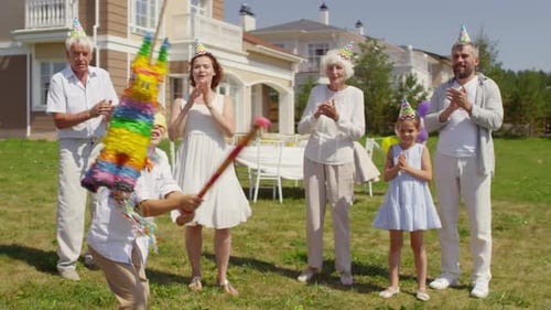 Little Boy Hitting Pinata with Bat at Family Party Outdoors