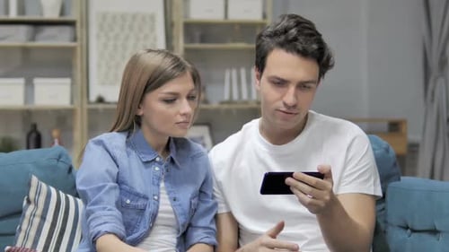 Excited Couple Watching Phone Content on Couch