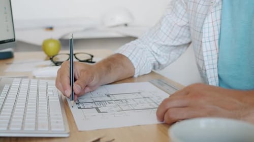 Closeup of Male Hands Working with Construction Plan While Architect is Busy in Office