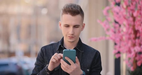 Young Smiling Man Using Mobile Phone in a Spring City