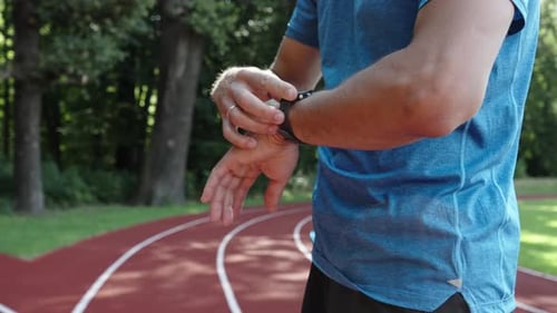 Man Checks Smart Watch on Outdoor Running Track