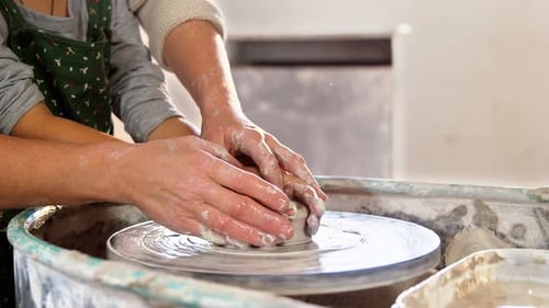 Child Learning Pottery with Adult Assistance at Wheel