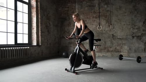 Attractive fitness woman riding exercise bike in gym. Slim lady on bike