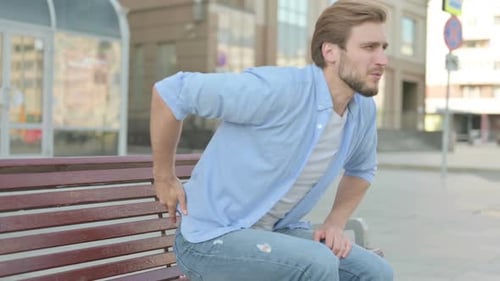 Young Man Sitting on Bench with Back Pain