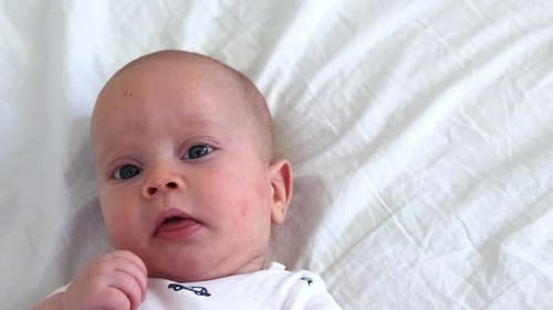 Close Up of Baby Lying on White Sheet Moving Arms Hands Looking Up Copy Space