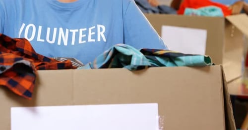 Voluntaria femenina con ropa en una caja de donación