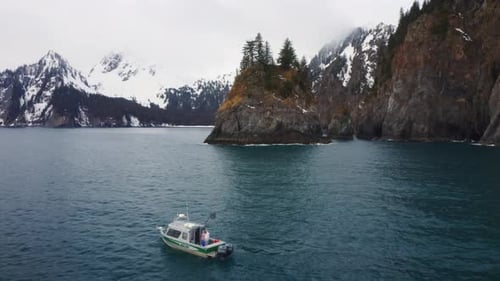 Boat Sailing Near Rocky Cliffs and Snowy Mountains