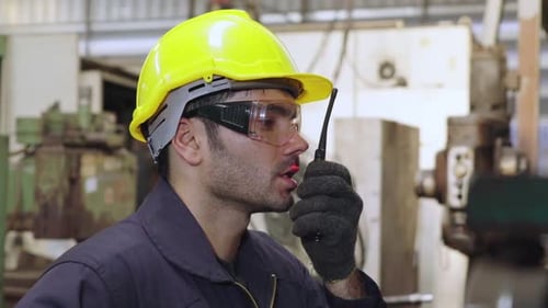 Fabrikarbeiter spricht mit tragbarem Radio, während er Maschinenteile inspiziert