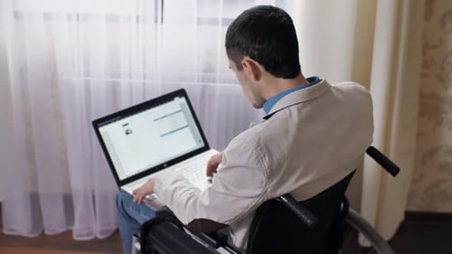 Man in Wheelchair Using Laptop by Window