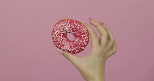 Woman's Hand Holding a Delicious Pink Frosted Donut