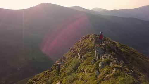 Hiker standing on top of rocky mountain enjoying magnificent view. Mountaineer looking at sunrise