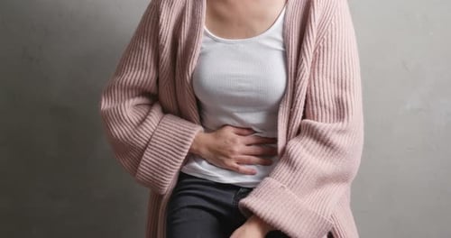 Woman Holding Stomach in Apparent Pain, Mid Shot