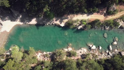 Narrow mountain river with clear turquoise water surrounded by rocky mountains and green trees.