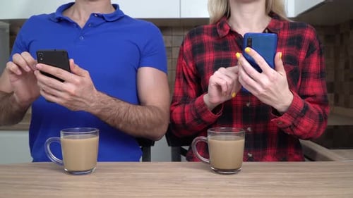 Couple Using Smartphones at Kitchen Table With Coffee