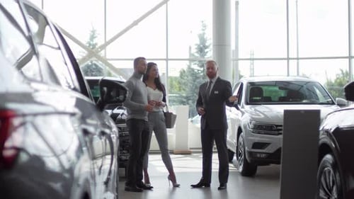 Couple Choosing New Car with Help of Salesman in Auto Showroom