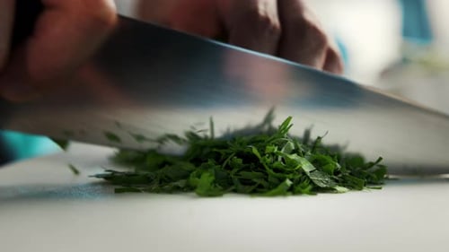 Professional kitchen of the restaurant, close-up: The chef cuts the greens herbs finely with a knife