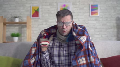 Un homme gelé couvert de givre enveloppé dans une couverture avec des gants dans le salon et regarde dans le