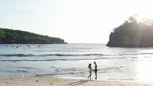 Man and Woman Walking Along Tropical Beach at Sunset, Tracking Aerial Shot of Young Couple