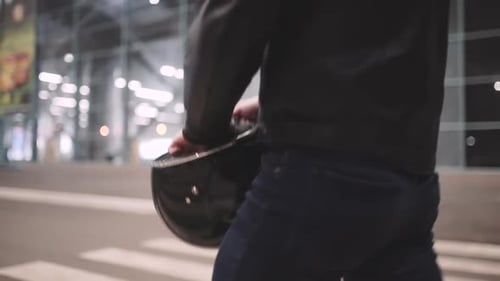 A Young Man Goes to His Motorcycle Sits on It and Puts a Helmet to Go on a Journey at Night Street