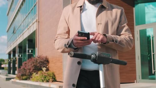 Man Using Phone with Scooter by Building