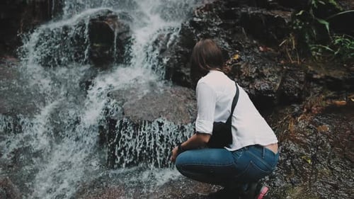 Woman Crouching by Beautiful Waterfall
