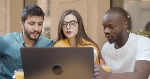 Three Adults Collaborating on a Laptop Outdoors