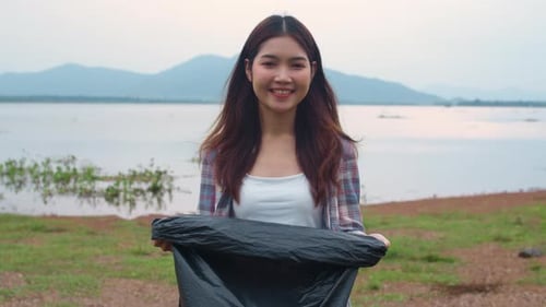 Woman Holds Trash Bag Near Lake and Mountains