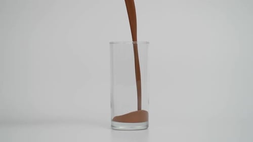 Super Slow Motion of Pouring Chocolate Milk in Glass Blue Background