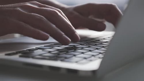 Hands and fingers typing on laptop computer keyboard in business corporate office