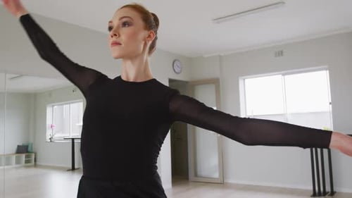 Caucasian female ballet dancer practicing ballet during a dance class in a bright studio