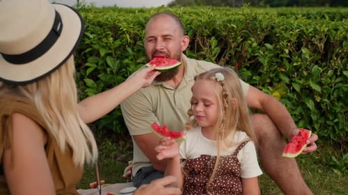 Family Enjoying Watermelon Picnic in Grassy Field
